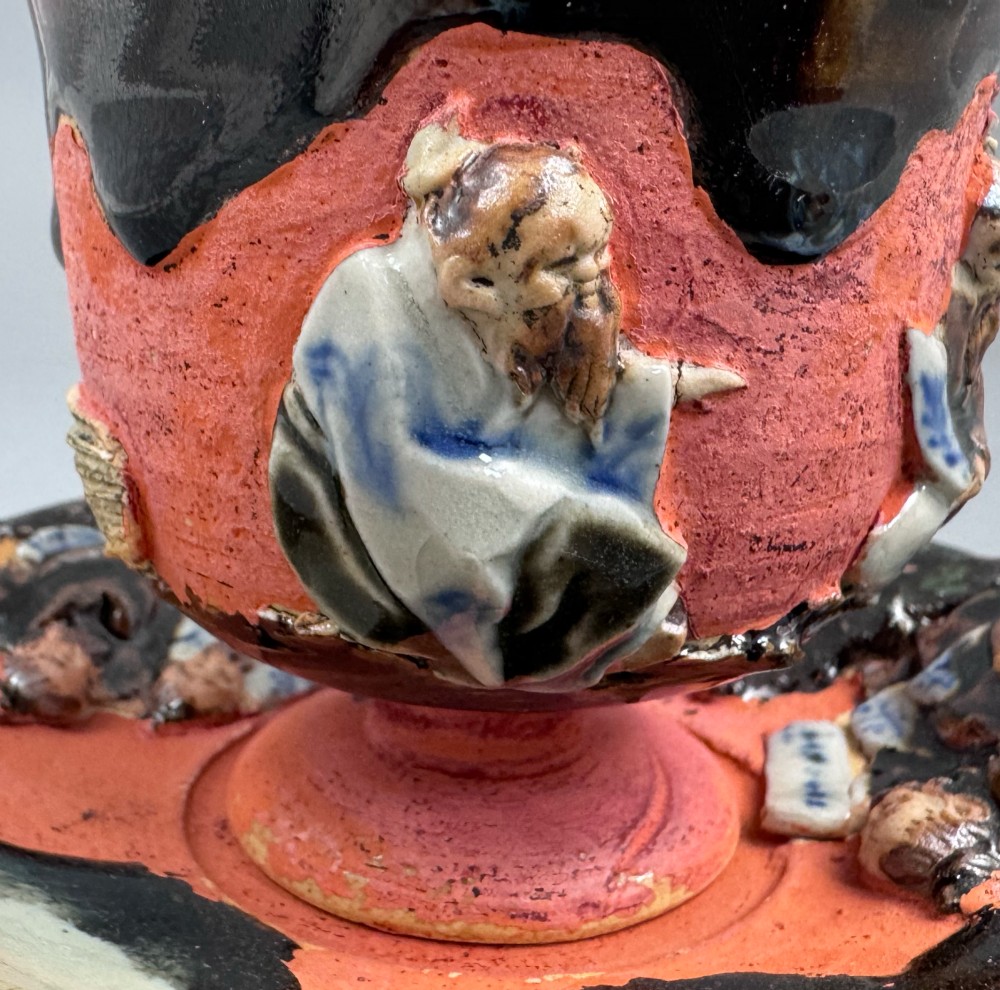 A Japanese Sumida Gawa teacup and saucer featuring relief-carved sage figures on a textured red background with a heavy dark flambe glaze. View VII