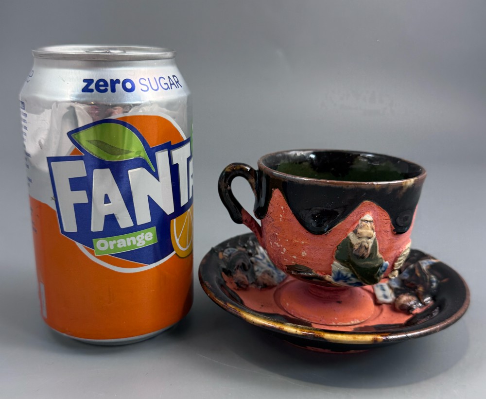 A Japanese Sumida Gawa teacup and saucer featuring relief-carved sage figures on a textured red background with a heavy dark flambe glaze. View VIII