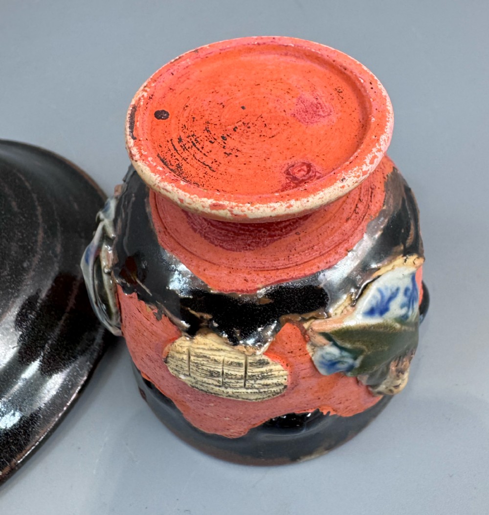 A Japanese Sumida Gawa teacup and saucer featuring relief-carved sage figures on a textured red background with a heavy dark flambe glaze. View IX