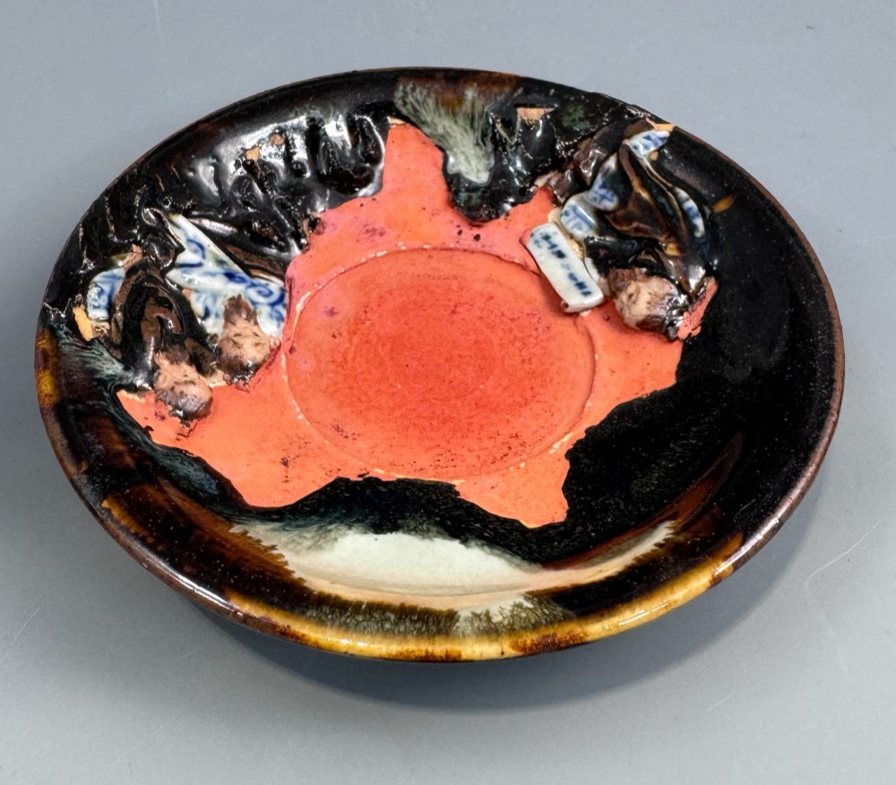 A Japanese Sumida Gawa teacup and saucer featuring relief-carved sage figures on a textured red background with a heavy dark flambe glaze. View X