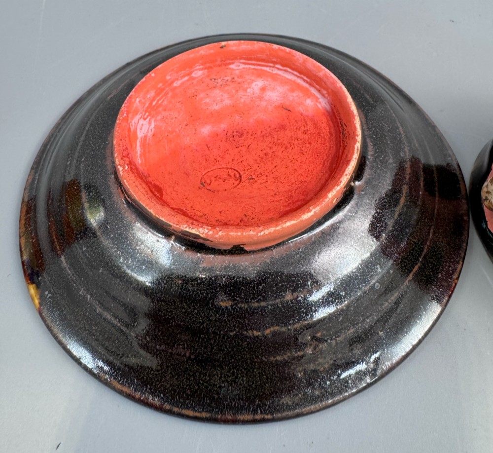 A Japanese Sumida Gawa teacup and saucer featuring relief-carved sage figures on a textured red background with a heavy dark flambe glaze. View XI