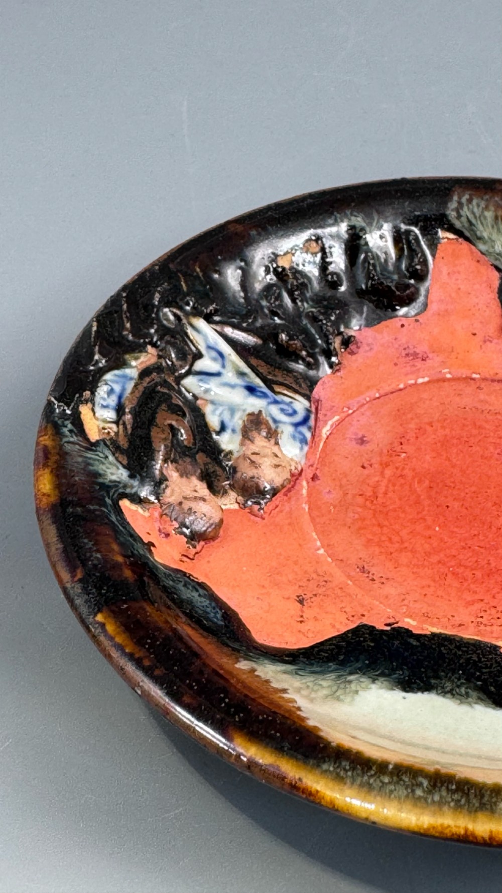 A Japanese Sumida Gawa teacup and saucer featuring relief-carved sage figures on a textured red background with a heavy dark flambe glaze. View XIII
