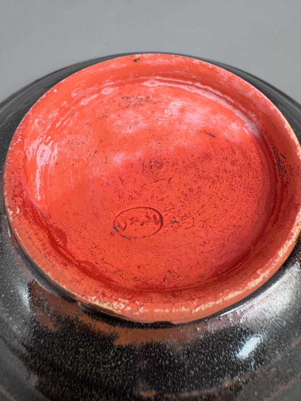A Japanese Sumida Gawa teacup and saucer featuring relief-carved sage figures on a textured red background with a heavy dark flambe glaze. View XIV