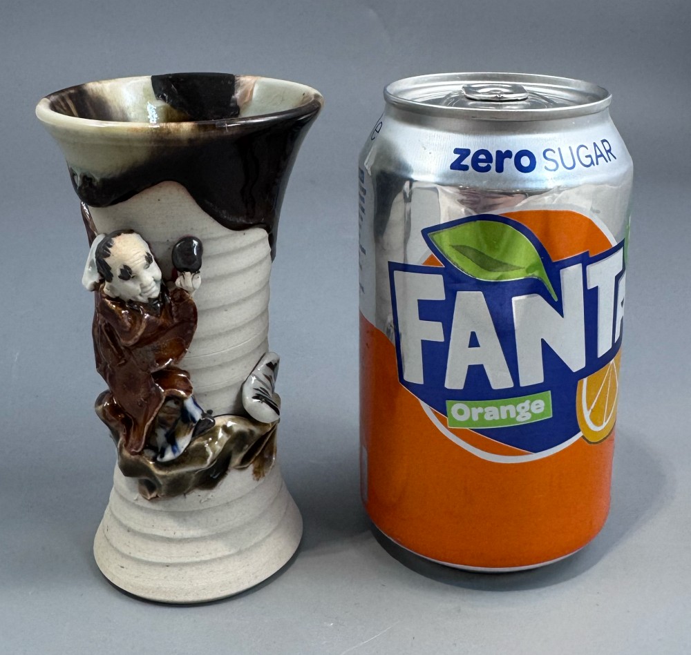 A Japanese Sumida Gawa stoneware vase featuring a ribbed cream body, dripping dark glaze along the flared rim, and an applied high-relief figure of a Rakan. View II
