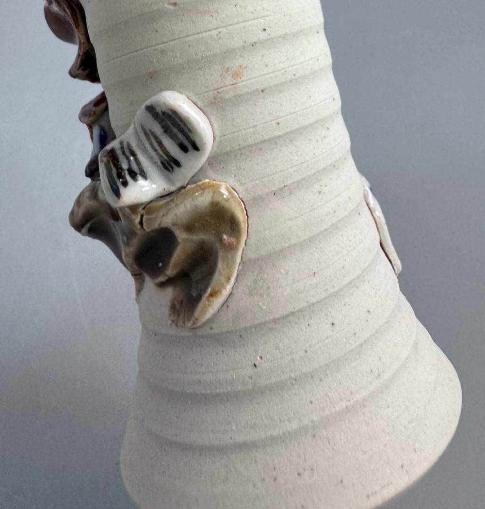 A Japanese Sumida Gawa stoneware vase featuring a ribbed cream body, dripping dark glaze along the flared rim, and an applied high-relief figure of a Rakan. View XIII
