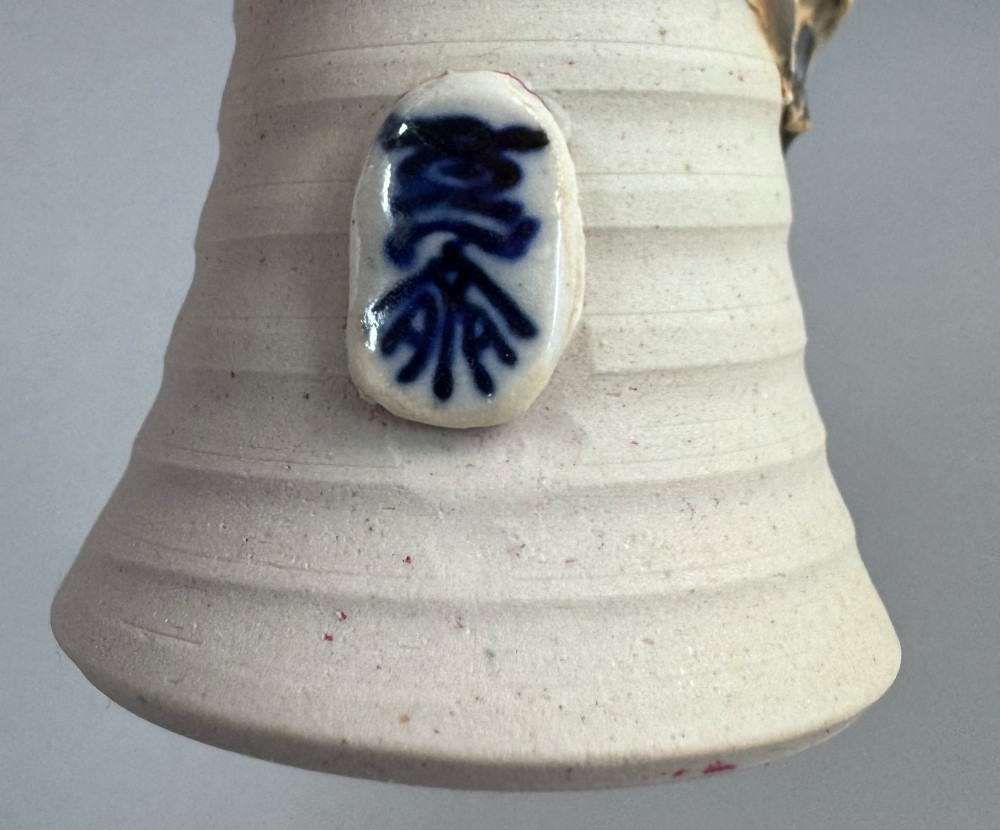 A Japanese Sumida Gawa stoneware vase featuring a ribbed cream body, dripping dark glaze along the flared rim, and an applied high-relief figure of a Rakan. View XIV