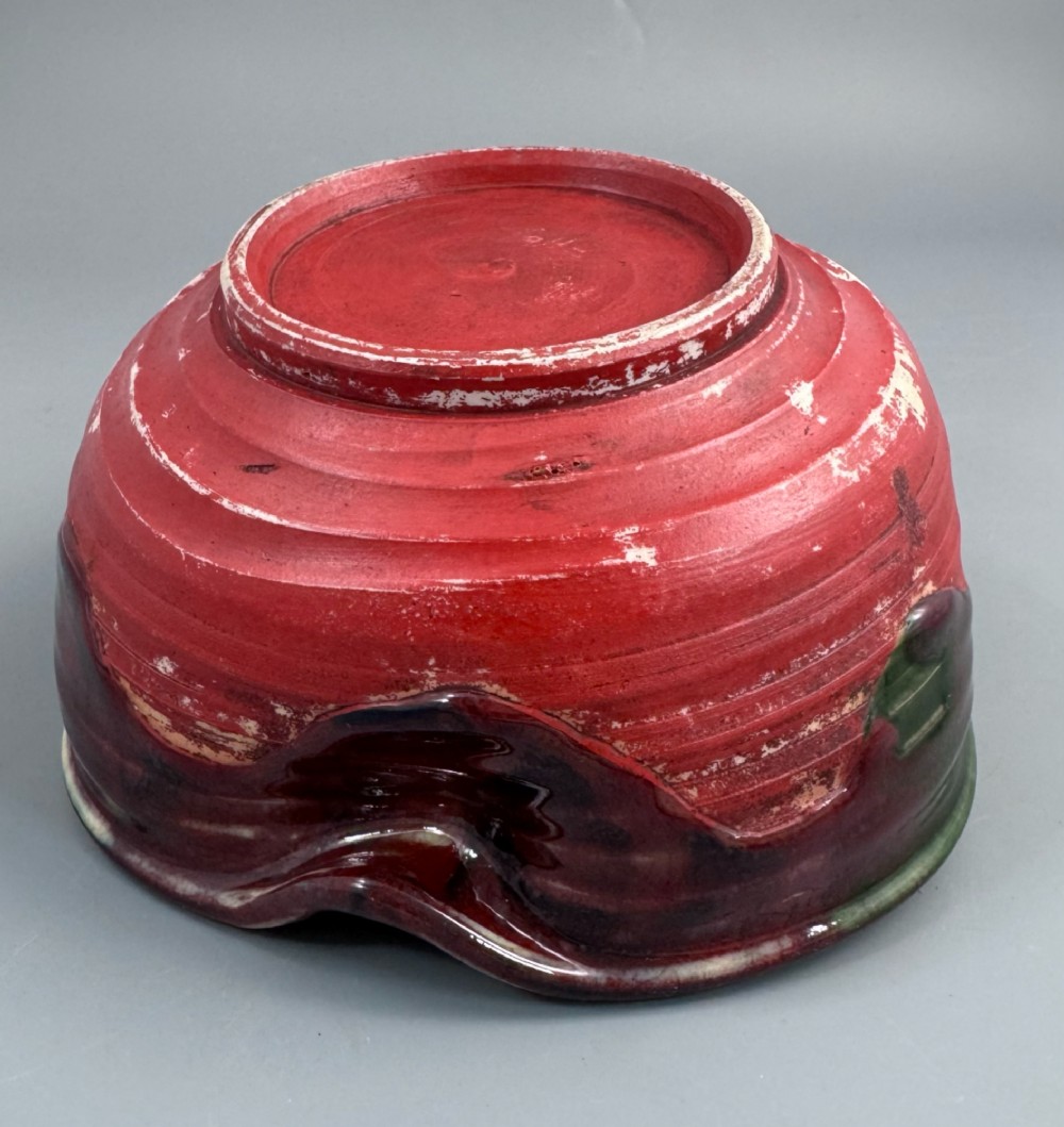 A Japanese Sumida Gawa pottery bowl featuring a dark green running glaze over a red base with two sculpted figures leaning over the rim and an applied white makers mark. View XI
