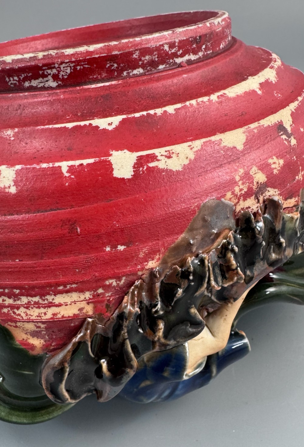 A Japanese Sumida Gawa pottery bowl featuring a dark green running glaze over a red base with two sculpted figures leaning over the rim and an applied white makers mark. View XII