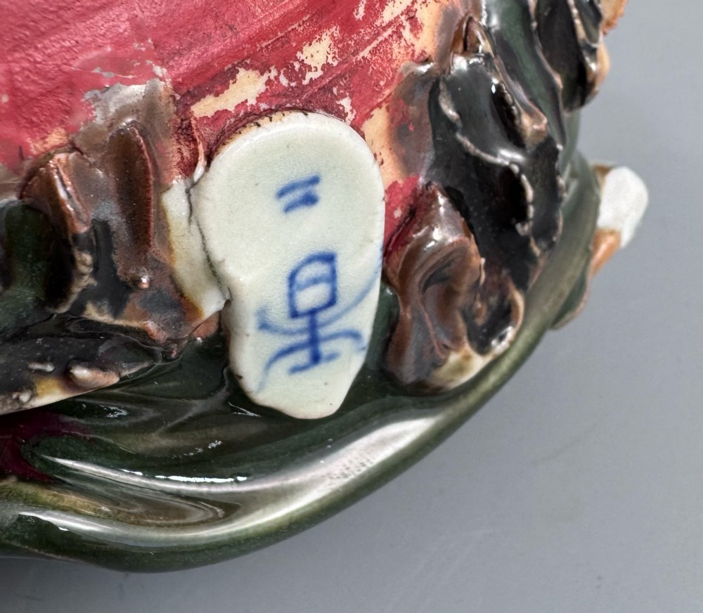 A Japanese Sumida Gawa pottery bowl featuring a dark green running glaze over a red base with two sculpted figures leaning over the rim and an applied white makers mark. View XIII
