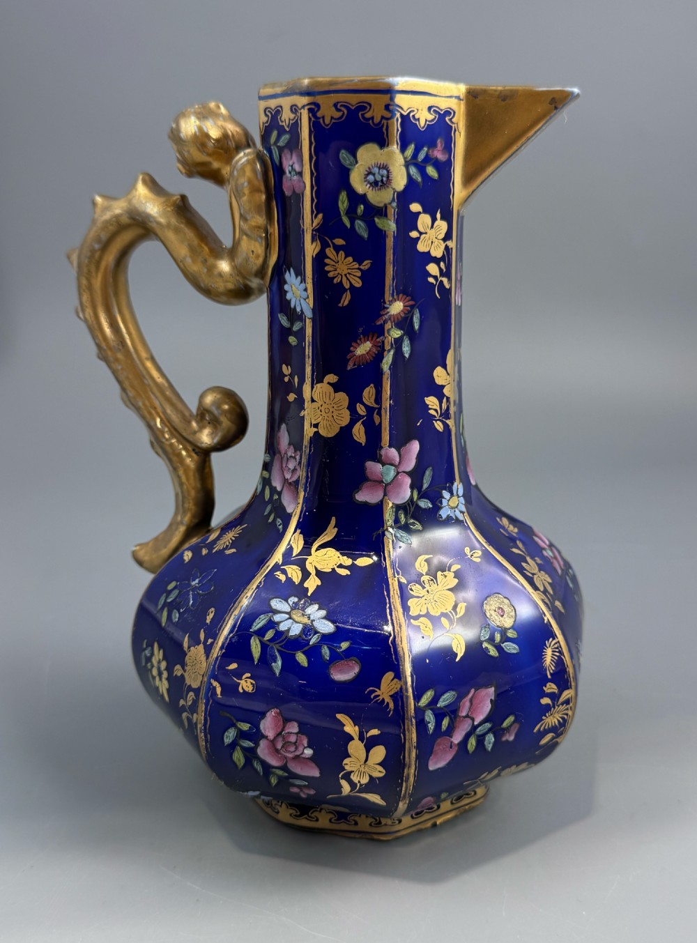 An octagonal cobalt blue ironstone ewer decorated with hand-painted Chinoiserie floral patterns and a gilded grotesque animal form handle.