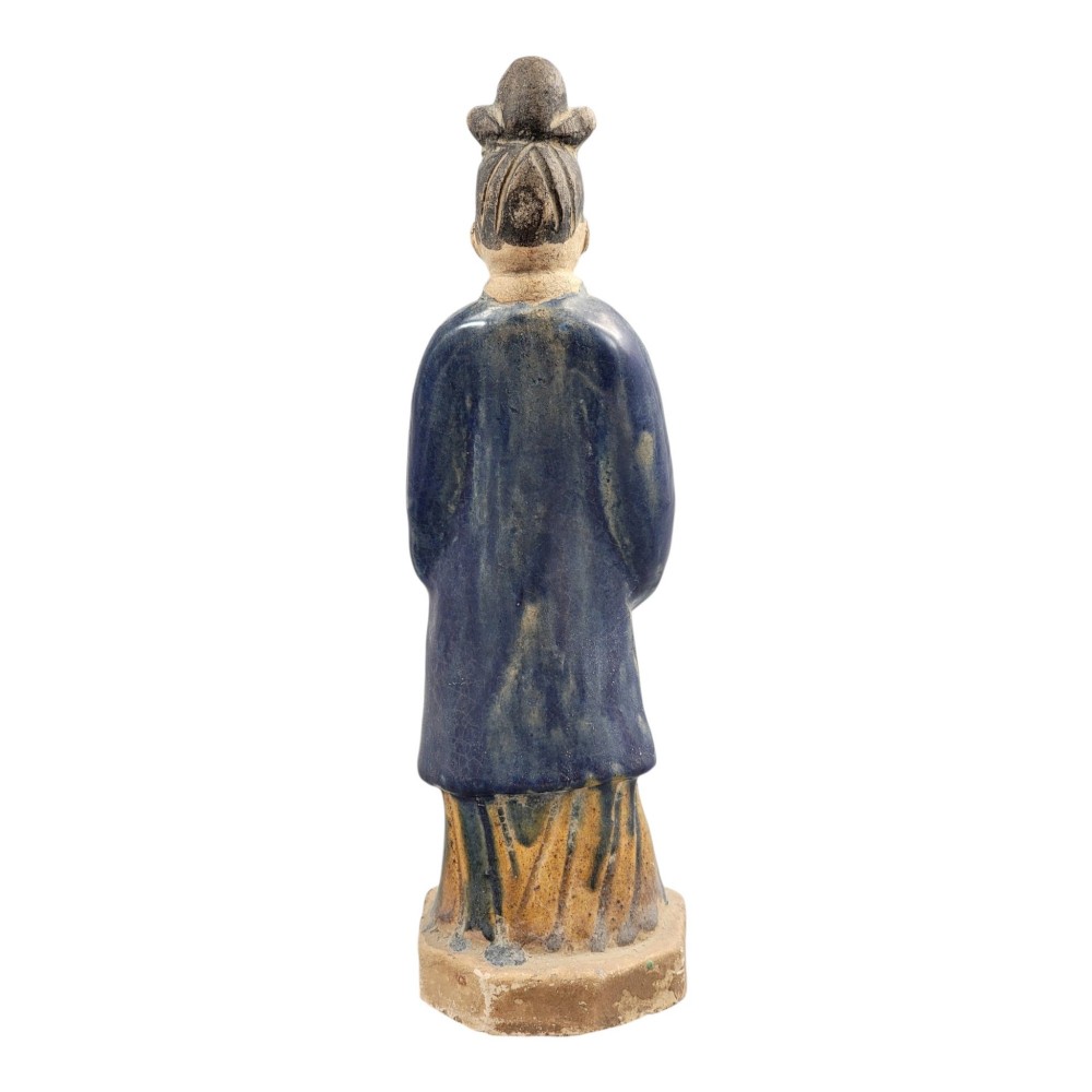 A Chinese Tang dynasty Sancai glazed earthenware figure of a court attendant standing on a hexagonal base with hands clasped under draped sleeves. View IV