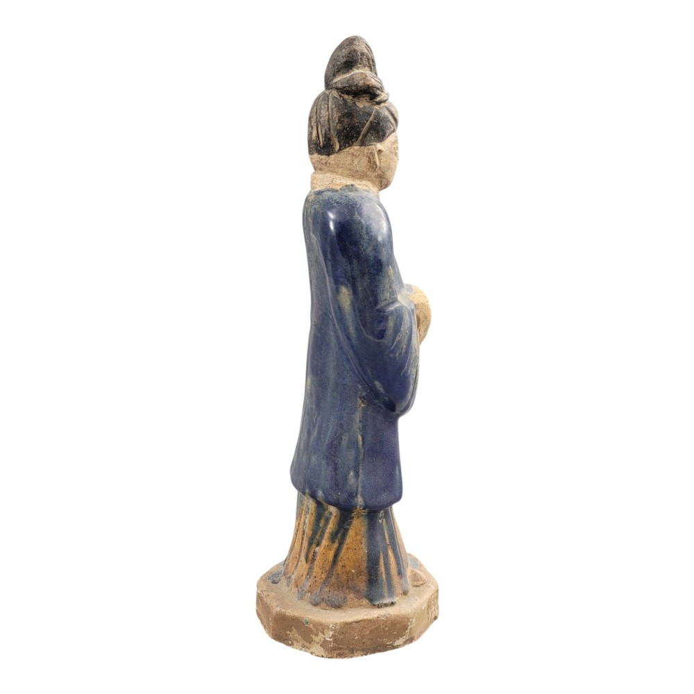 A Chinese Tang dynasty Sancai glazed earthenware figure of a court attendant standing on a hexagonal base with hands clasped under draped sleeves. View V
