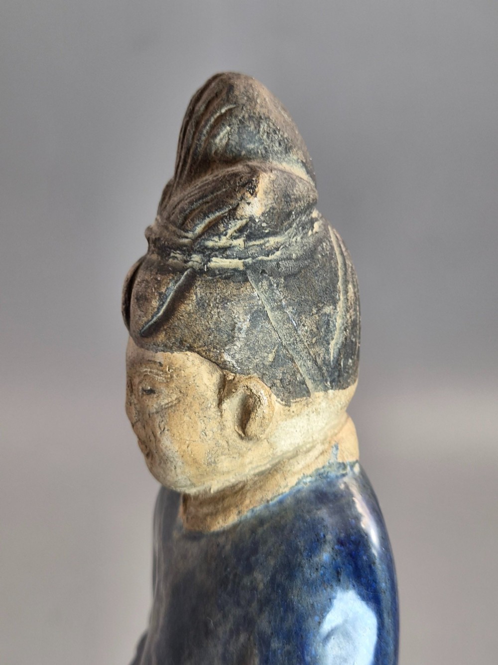 A Chinese Tang dynasty Sancai glazed earthenware figure of a court attendant standing on a hexagonal base with hands clasped under draped sleeves. View XI