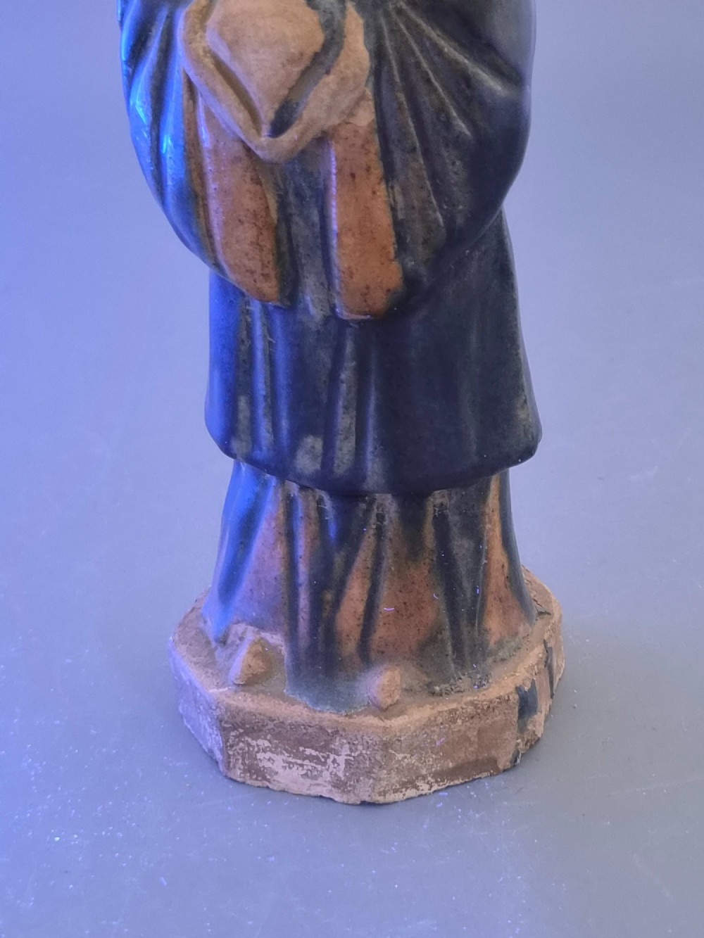 A Chinese Tang dynasty Sancai glazed earthenware figure of a court attendant standing on a hexagonal base with hands clasped under draped sleeves. View XIII