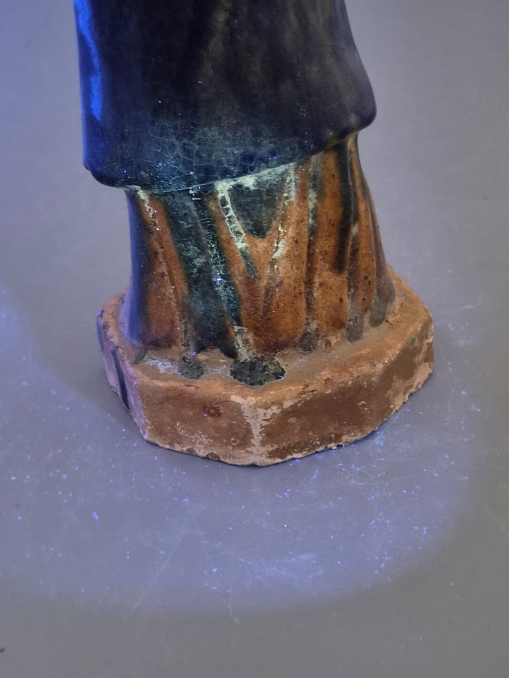 A Chinese Tang dynasty Sancai glazed earthenware figure of a court attendant standing on a hexagonal base with hands clasped under draped sleeves. View XIV
