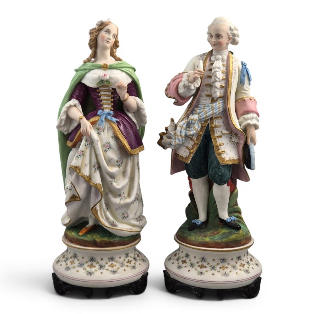 A pair of French biscuit porcelain figures depicting a male and female figure in 18th-century court costume with polychrome enamelled details.