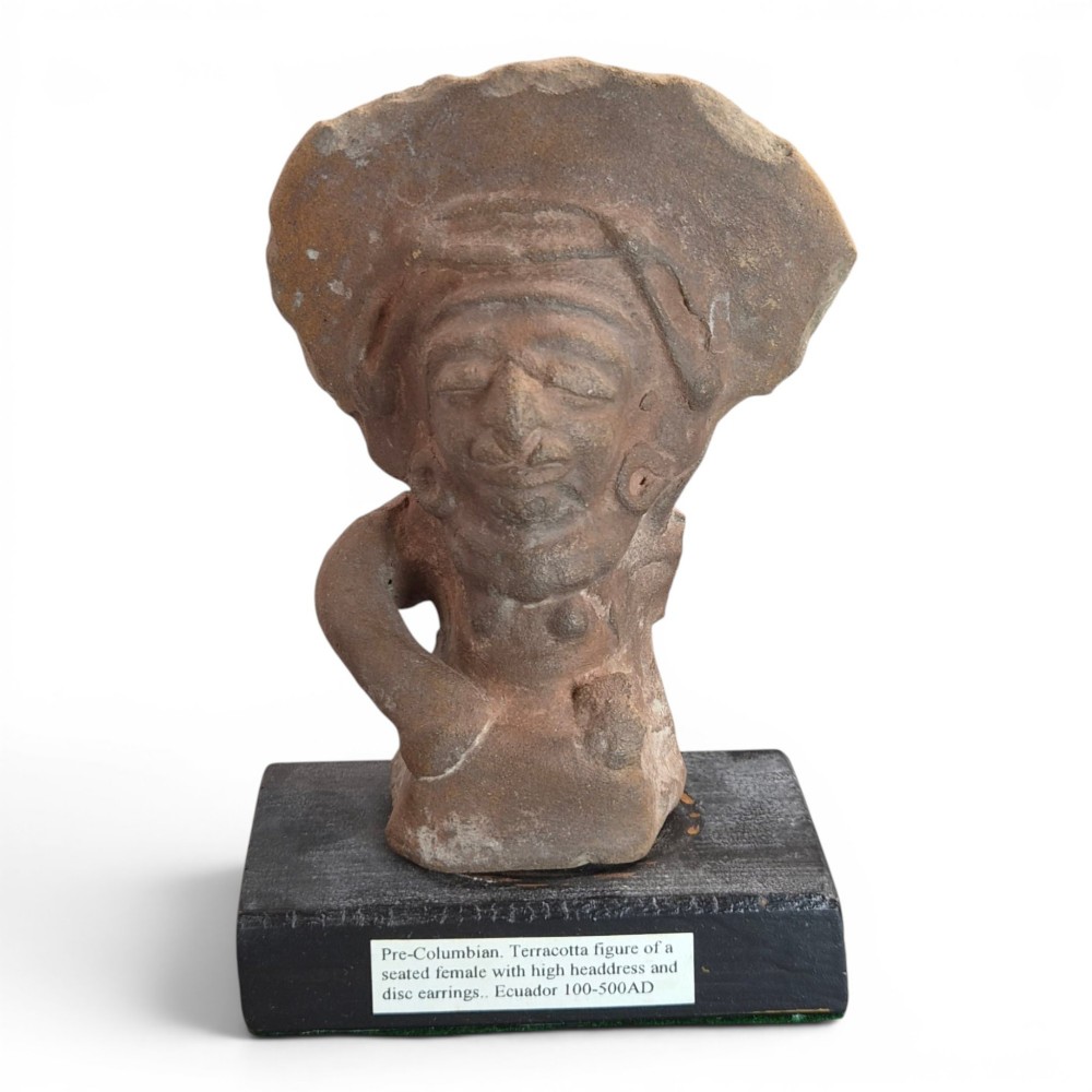 A Pre-Columbian earthenware terracotta sculpture depicting a seated female figure with a flared headdress, mounted on a rectangular dark wooden base.