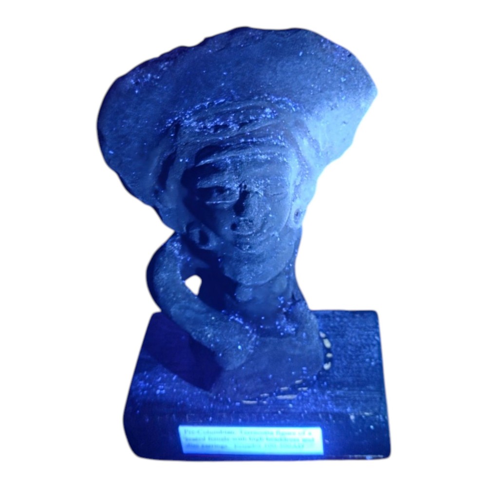 A Pre-Columbian earthenware terracotta sculpture depicting a seated female figure with a flared headdress, mounted on a rectangular dark wooden base. View X