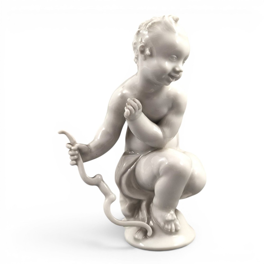 A glazed white porcelain figurine depicting a crouching winged cherub holding a curved bow on a circular base.