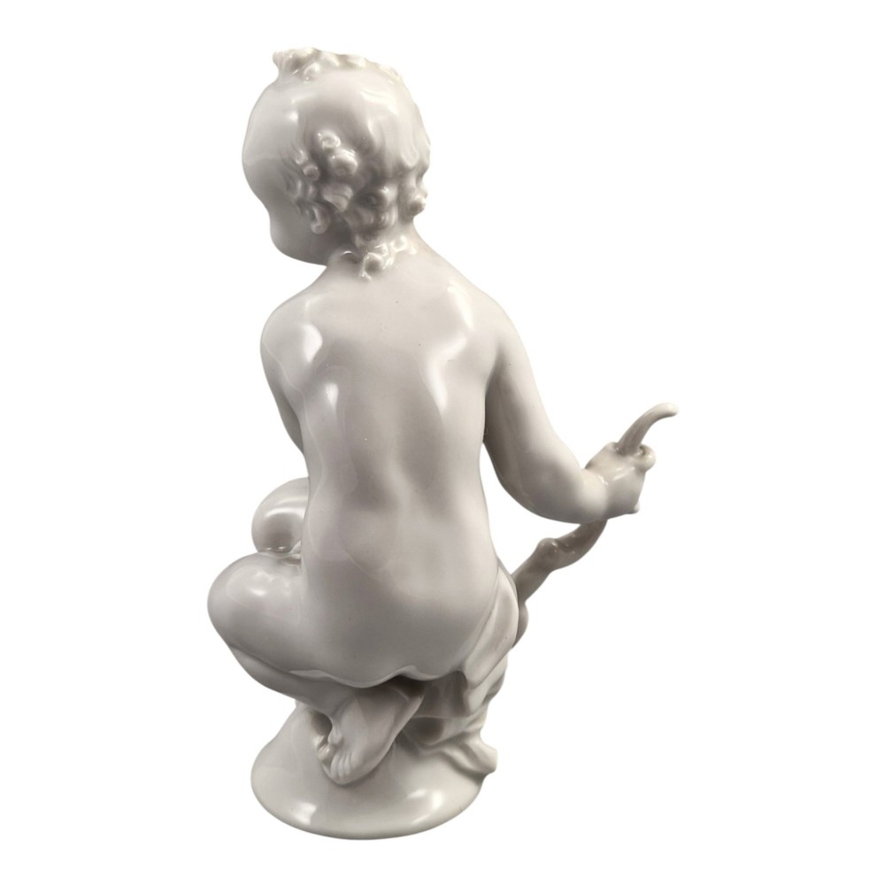 A glazed white porcelain figurine depicting a crouching winged cherub holding a curved bow on a circular base. View IV