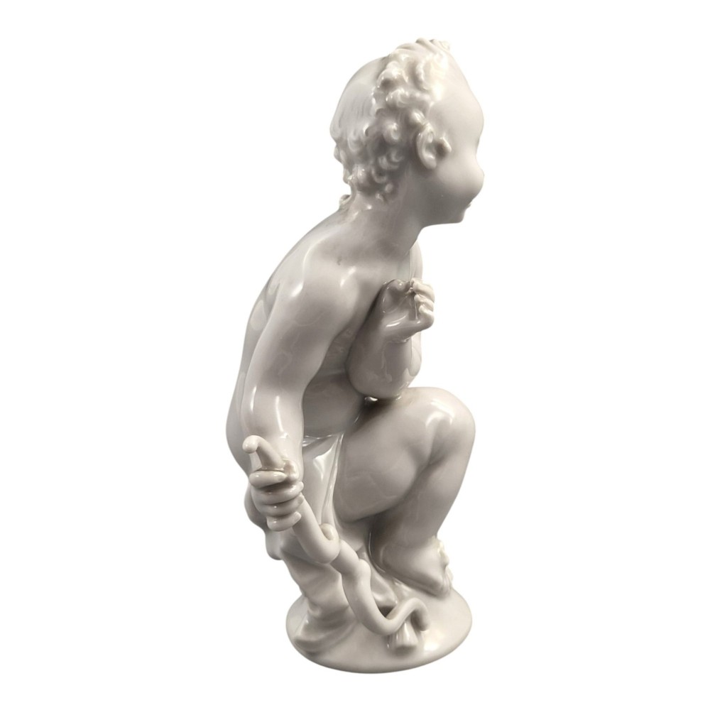A glazed white porcelain figurine depicting a crouching winged cherub holding a curved bow on a circular base. View VI