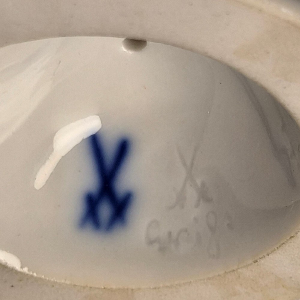 A glazed white porcelain figurine depicting a crouching winged cherub holding a curved bow on a circular base. View IX