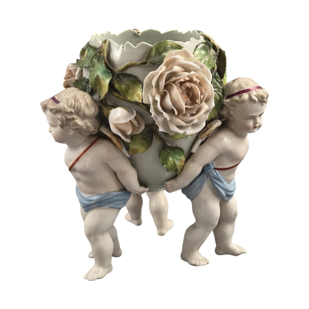 A German Sitzendorf porcelain egg-shaped vase featuring applied green leaves, pale pink roses, and three cherub figures supporting the base. View II