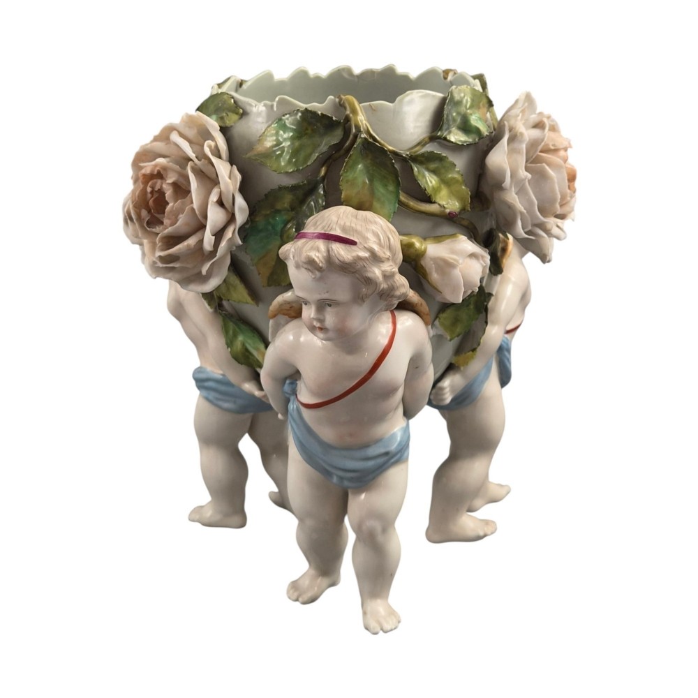 A German Sitzendorf porcelain egg-shaped vase featuring applied green leaves, pale pink roses, and three cherub figures supporting the base. View III