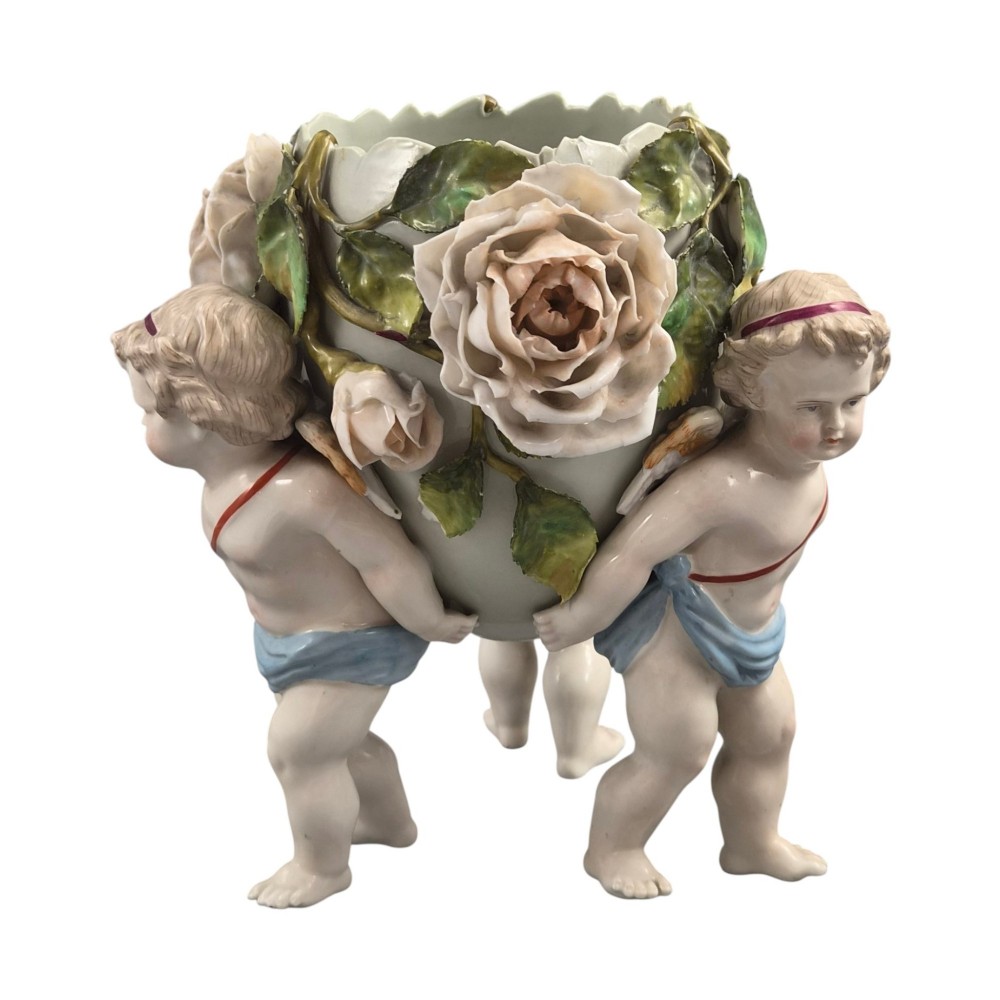 A German Sitzendorf porcelain egg-shaped vase featuring applied green leaves, pale pink roses, and three cherub figures supporting the base. View IV