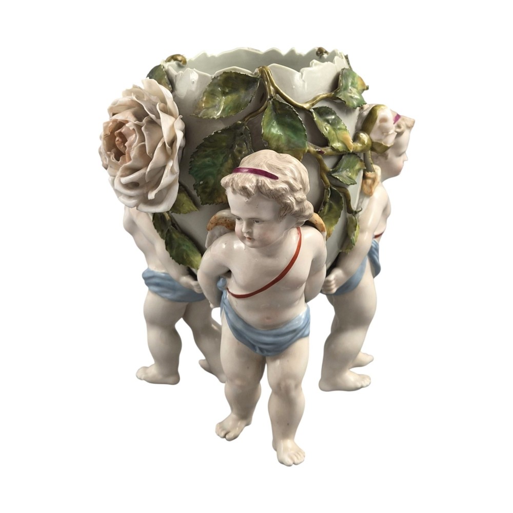 A German Sitzendorf porcelain egg-shaped vase featuring applied green leaves, pale pink roses, and three cherub figures supporting the base. View V