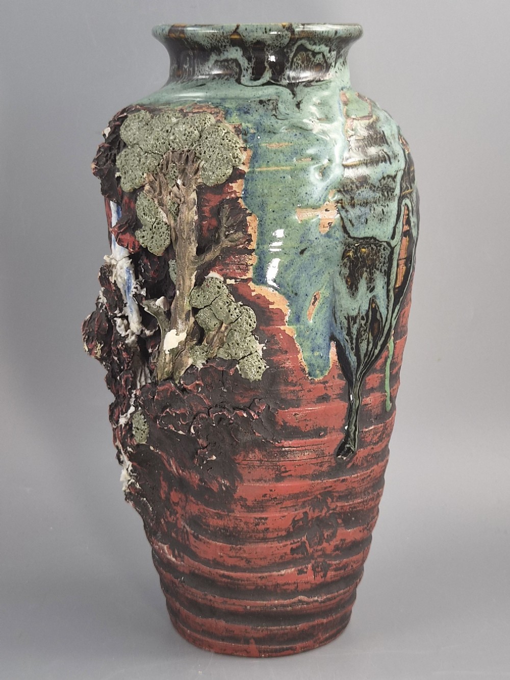 A Japanese Sumida Gawa stoneware vase featuring high-relief sculptures of a stag, waterfall, and tree against a ribbed dark red base with a green drip glaze top rim. View II