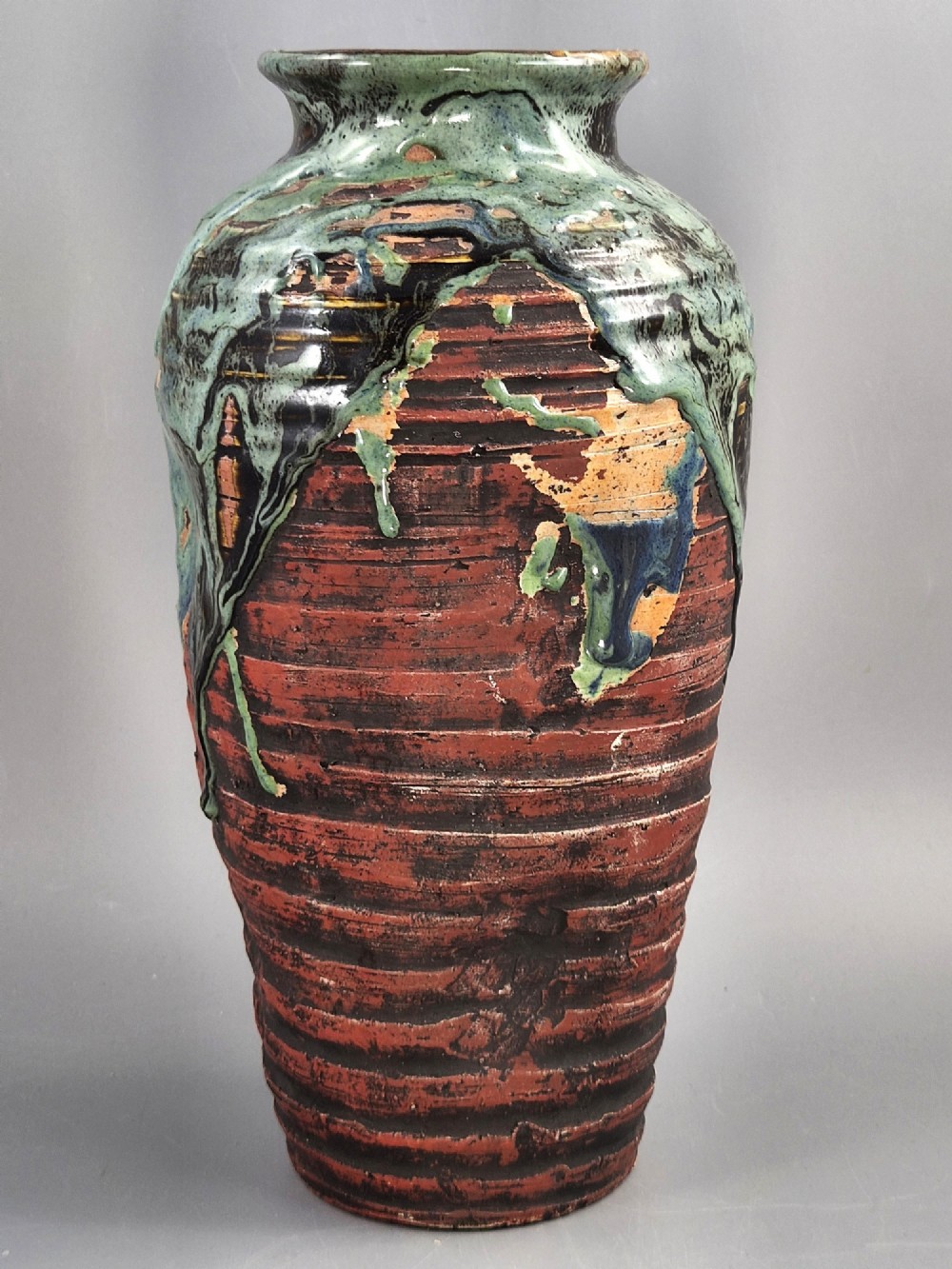 A Japanese Sumida Gawa stoneware vase featuring high-relief sculptures of a stag, waterfall, and tree against a ribbed dark red base with a green drip glaze top rim. View IV