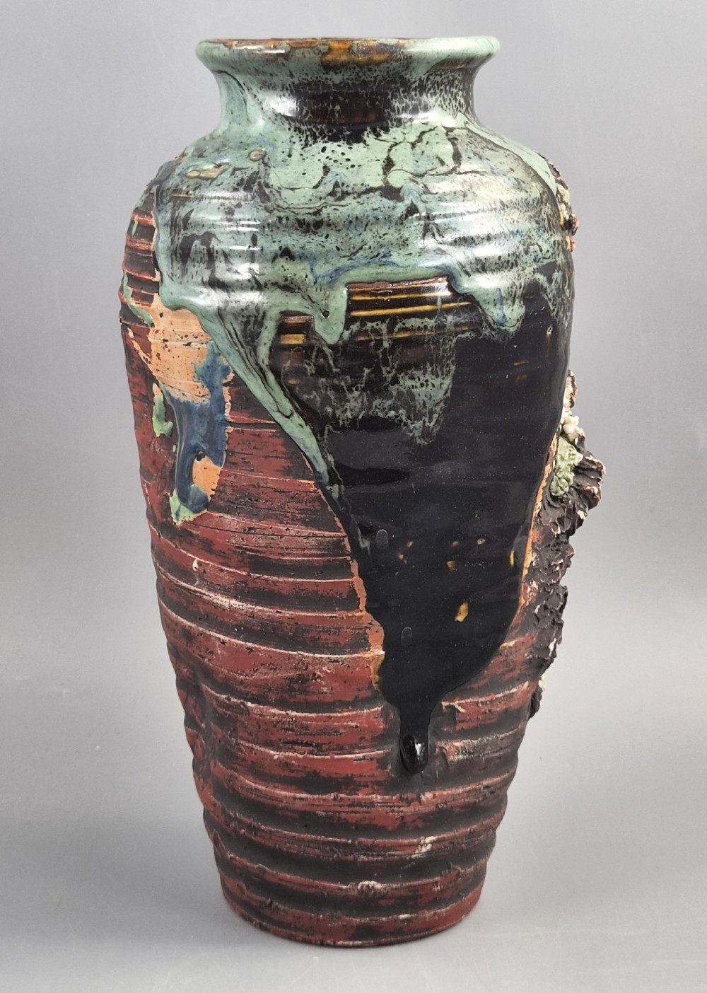 A Japanese Sumida Gawa stoneware vase featuring high-relief sculptures of a stag, waterfall, and tree against a ribbed dark red base with a green drip glaze top rim. View V