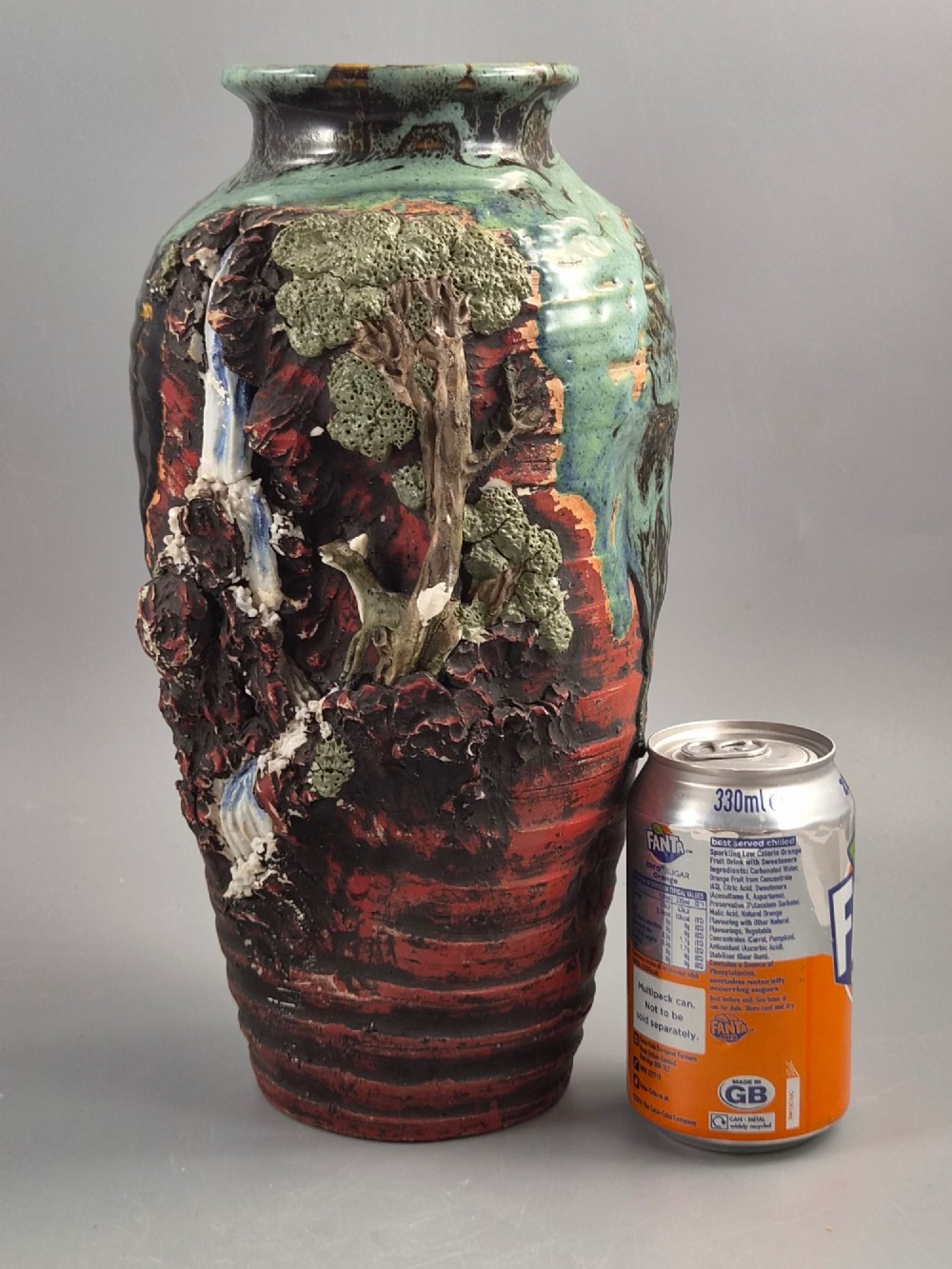 A Japanese Sumida Gawa stoneware vase featuring high-relief sculptures of a stag, waterfall, and tree against a ribbed dark red base with a green drip glaze top rim. View IX