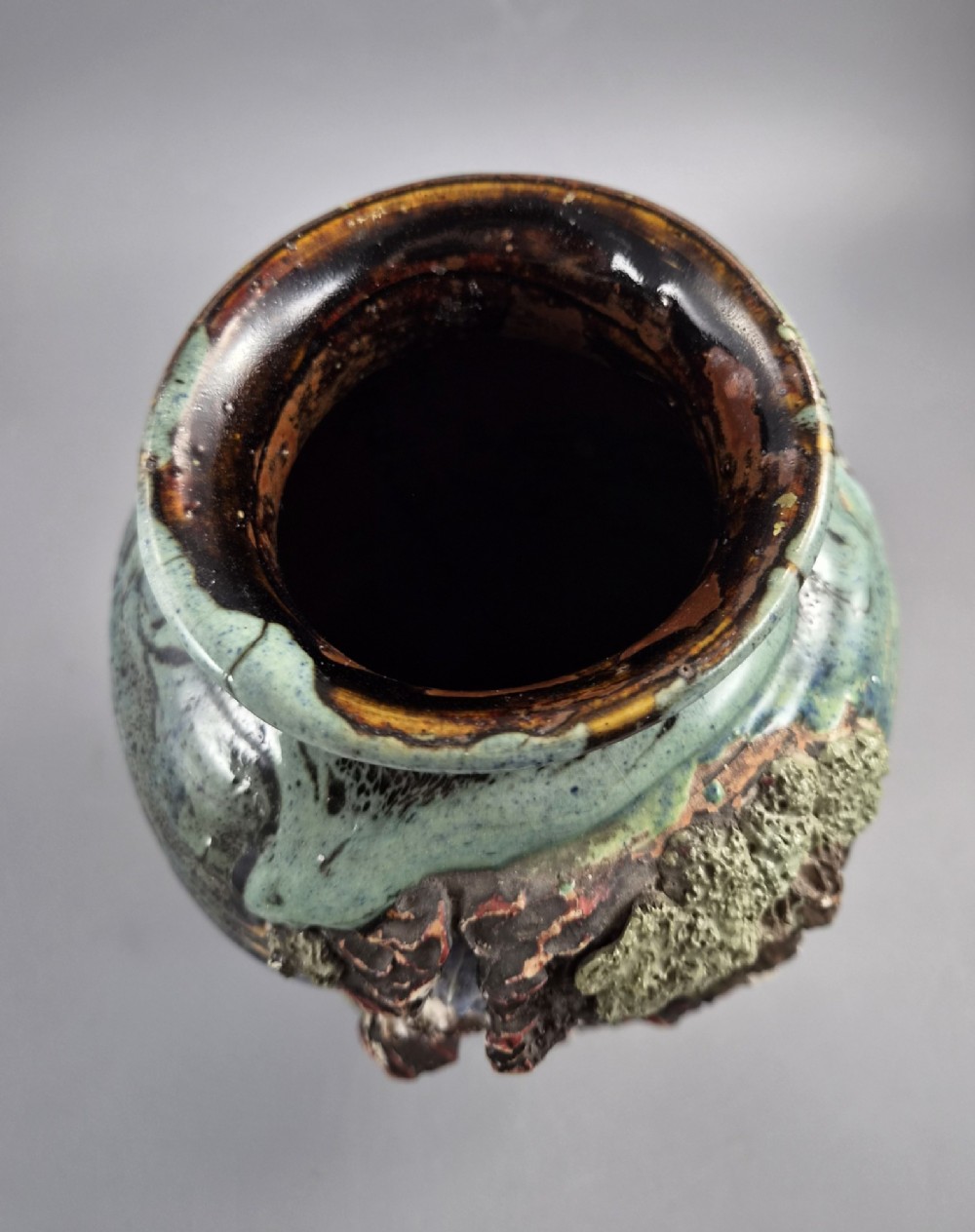 A Japanese Sumida Gawa stoneware vase featuring high-relief sculptures of a stag, waterfall, and tree against a ribbed dark red base with a green drip glaze top rim. View X