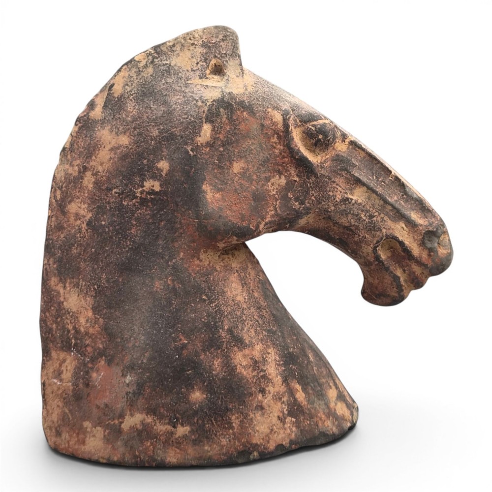 A painted terracotta sculpture depicting the profile of a horse head with earthy red and dark charcoal surface pigments.