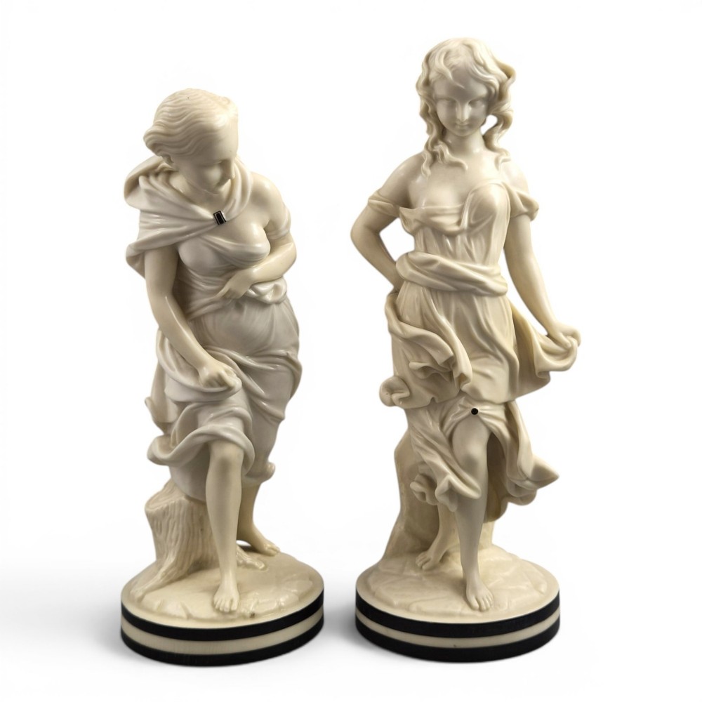 A pair of Victorian cream-glazed porcelain figures depicting classical female forms with flowing drapery set on circular bases.