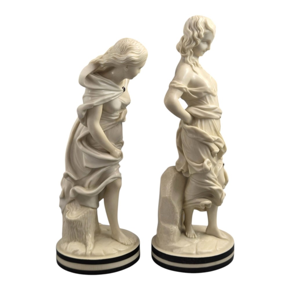 A pair of Victorian cream-glazed porcelain figures depicting classical female forms with flowing drapery set on circular bases. View V