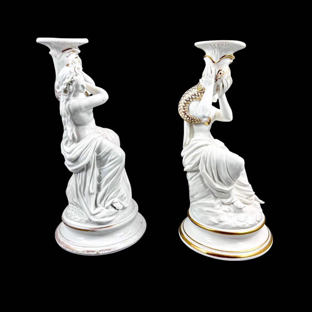 A pair of white glazed porcelain candlesticks featuring sculpted classical female figures holding urn-shaped sconces with gilt trim on circular bases. View II
