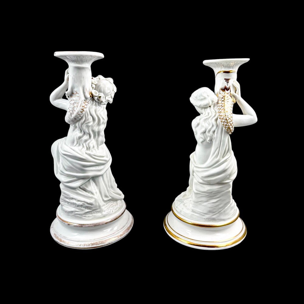 A pair of white glazed porcelain candlesticks featuring sculpted classical female figures holding urn-shaped sconces with gilt trim on circular bases. View III