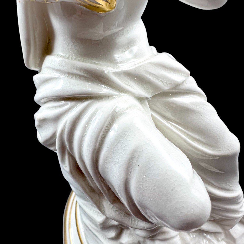 A pair of white glazed porcelain candlesticks featuring sculpted classical female figures holding urn-shaped sconces with gilt trim on circular bases. View VII