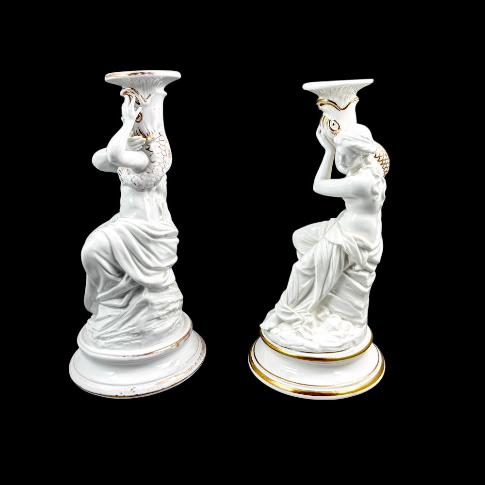 A pair of white glazed porcelain candlesticks featuring sculpted classical female figures holding urn-shaped sconces with gilt trim on circular bases. View VIII