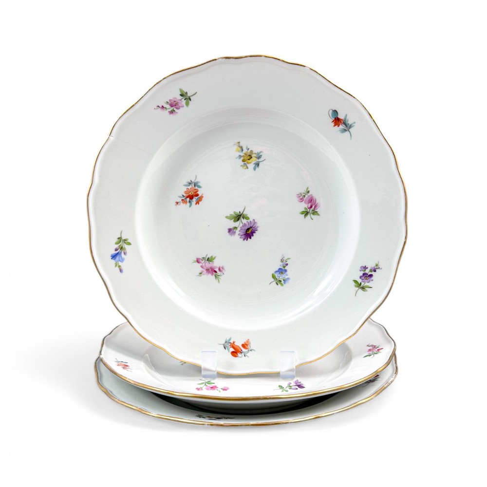 A set of three white hard-paste porcelain plates decorated with hand-painted scattered floral sprigs and scalloped gilded edges.