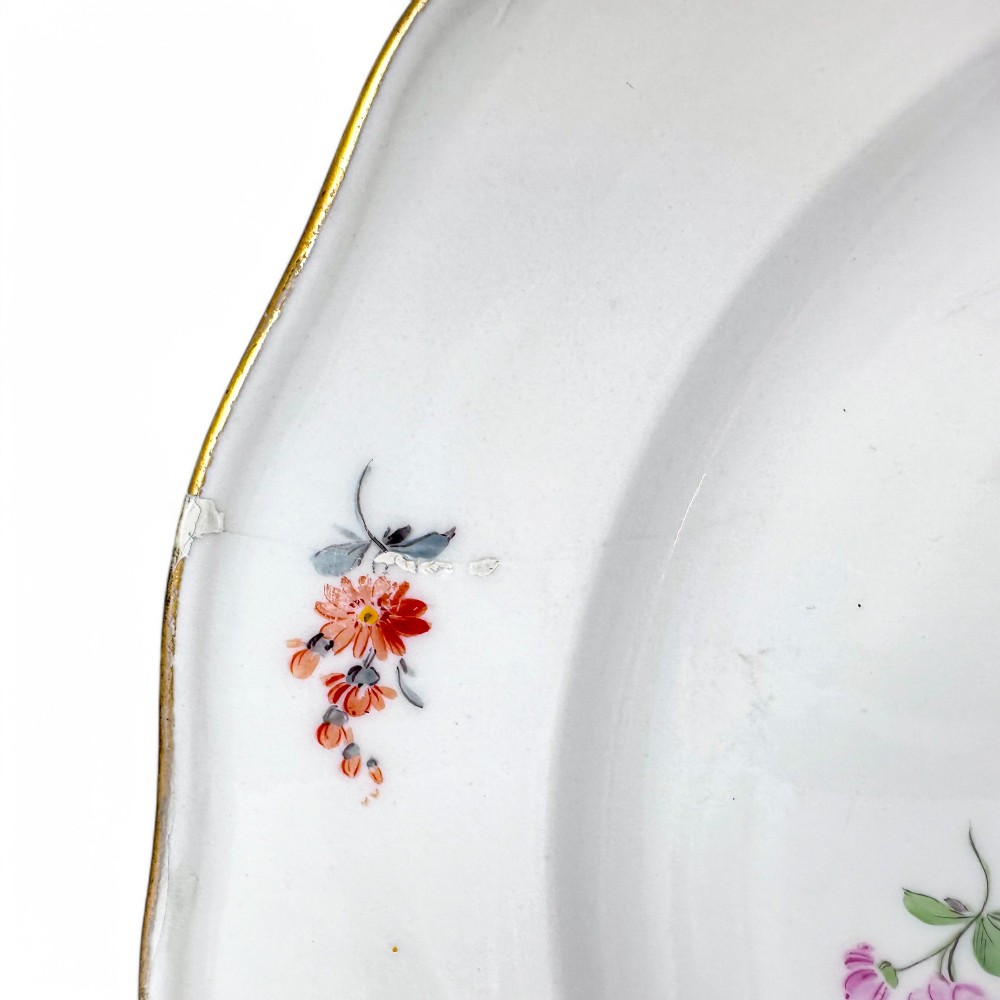 A set of three white hard-paste porcelain plates decorated with hand-painted scattered floral sprigs and scalloped gilded edges. View X