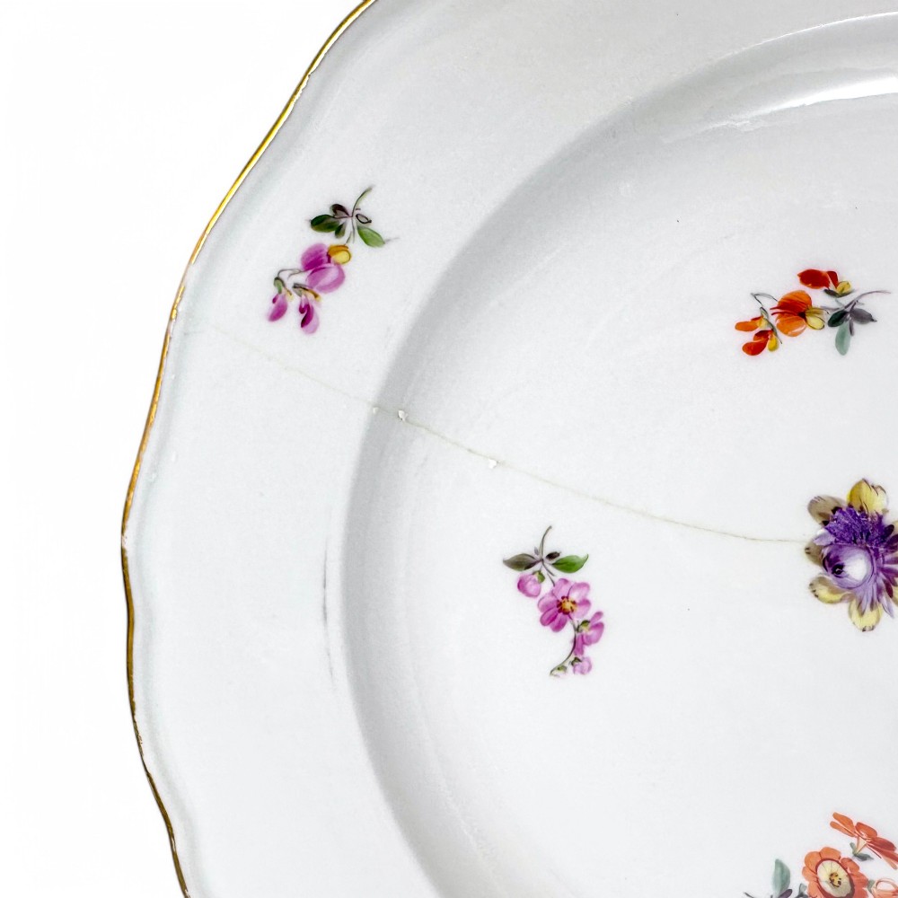 A set of three white hard-paste porcelain plates decorated with hand-painted scattered floral sprigs and scalloped gilded edges. View XV