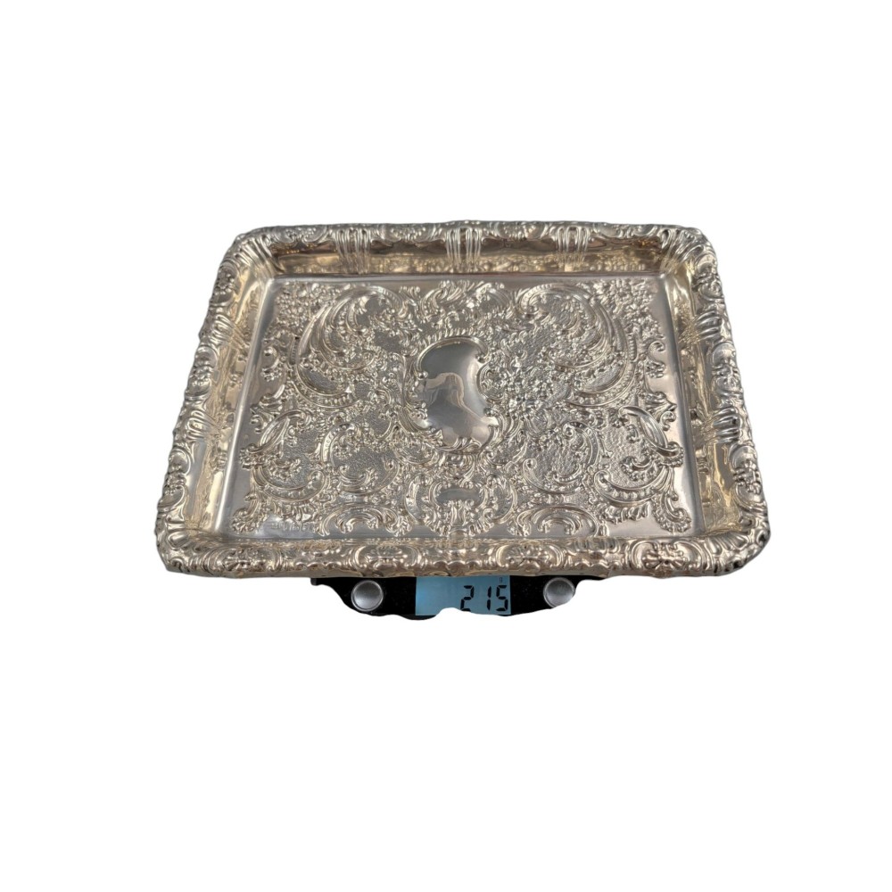 A rectangular Edwardian sterling silver card tray with intricate floral repousse scrollwork detailing, a plain central cartouche, and a raised scalloped rim. View IV