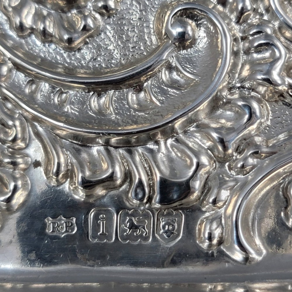 A rectangular Edwardian sterling silver card tray with intricate floral repousse scrollwork detailing, a plain central cartouche, and a raised scalloped rim. View V