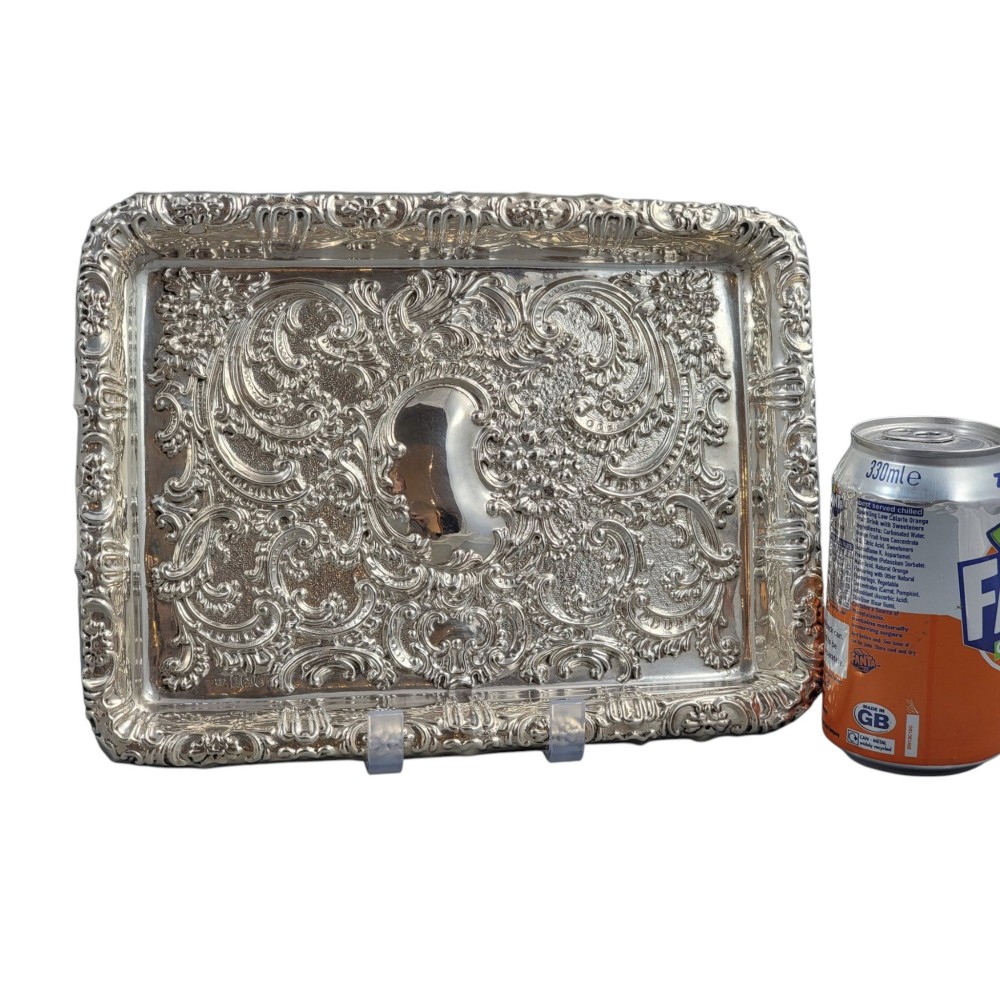 A rectangular Edwardian sterling silver card tray with intricate floral repousse scrollwork detailing, a plain central cartouche, and a raised scalloped rim. View VI