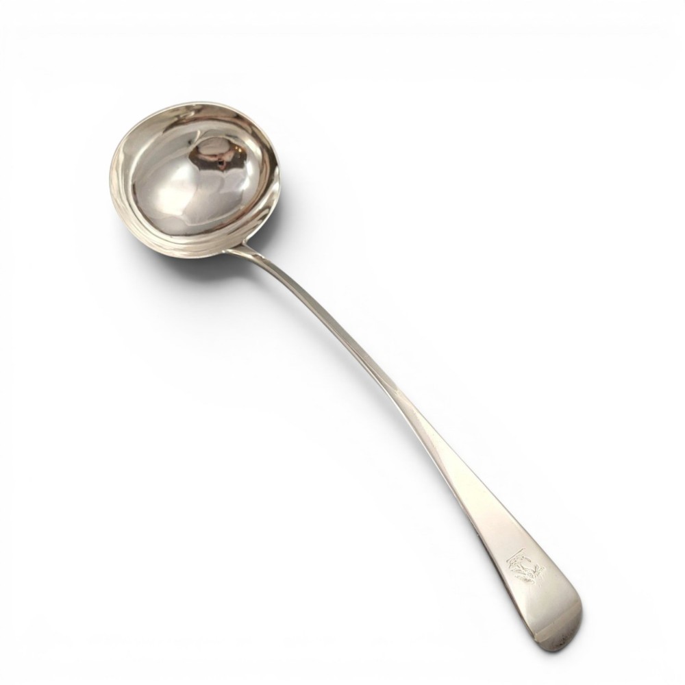 A Georgian sterling silver soup ladle featuring a deep circular bowl, a long curved stem in the Old English pattern, and an engraved crest near the handle tip.