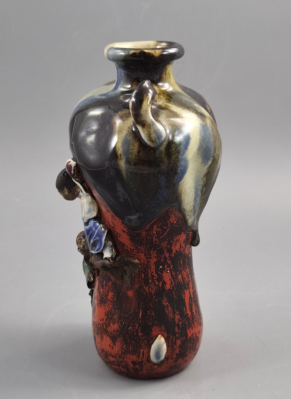 A Japanese Sumida Gawa pottery vase featuring an asymmetrical spouted form with a dark flambe drip glaze over a textured red lower body adorned with applied high-relief figures of boys. View III